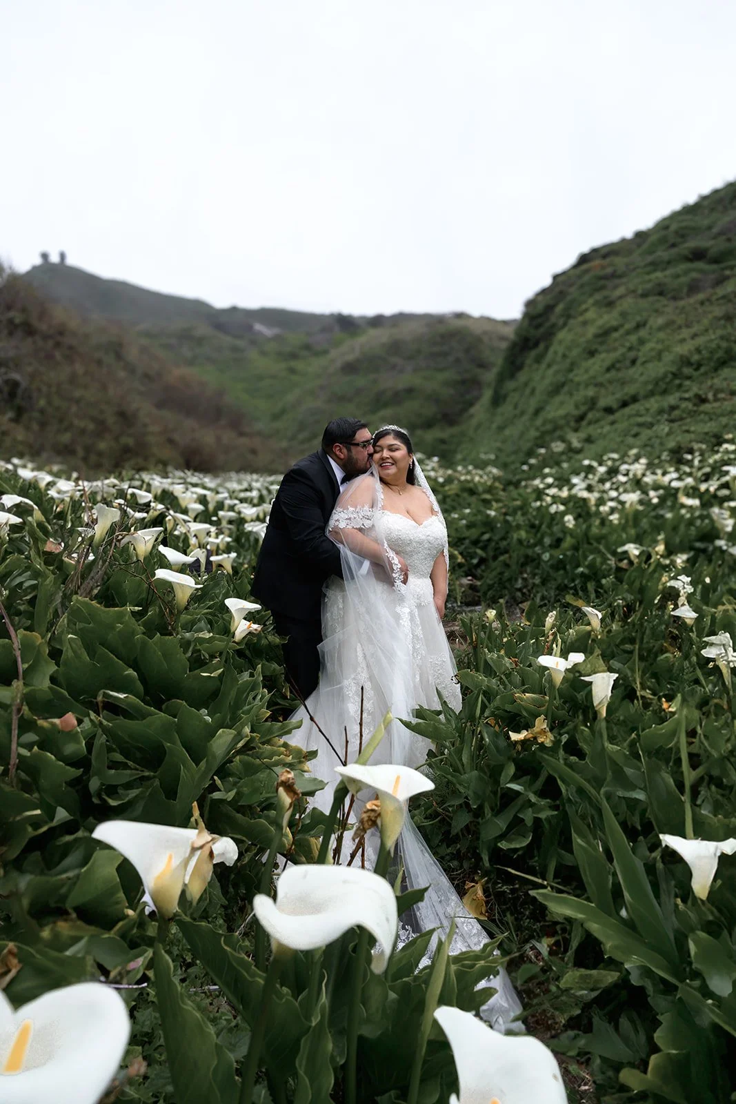 a bride and groom surrounded by calla lilies in big sur