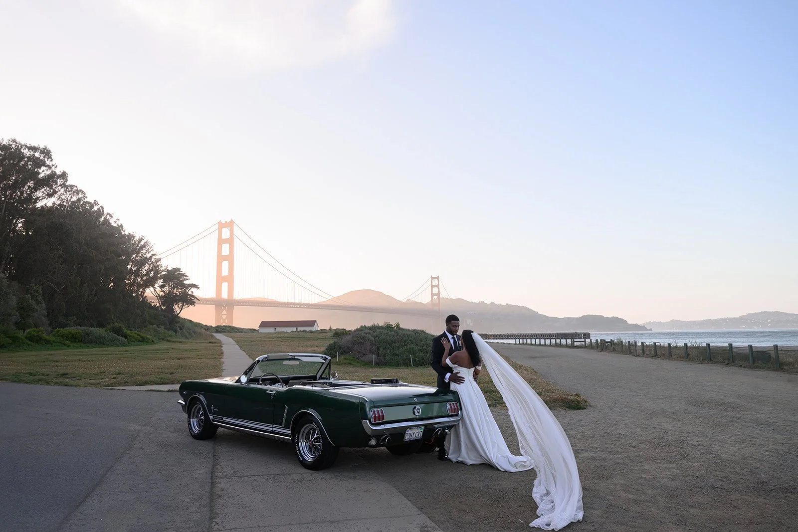 a bride and groom with a classic car in front of the Golden Gate Bridge