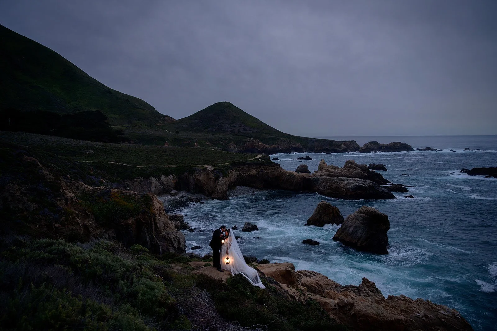 Bride and groom on a cliffside in big sur at night time with lanterns