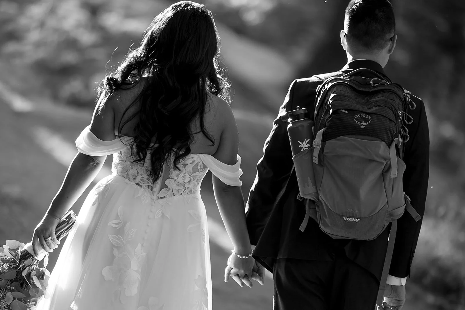 a photo of a bride and groom hiking with a backpack in their wedding outfits in black and white