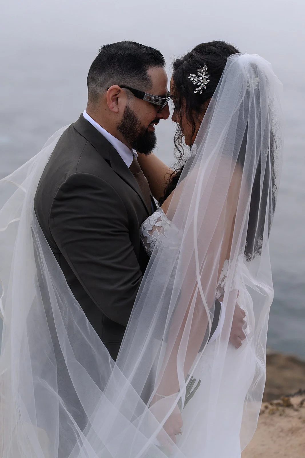 a bride and groom on a cliffside in big sur on their wedding day under a veil