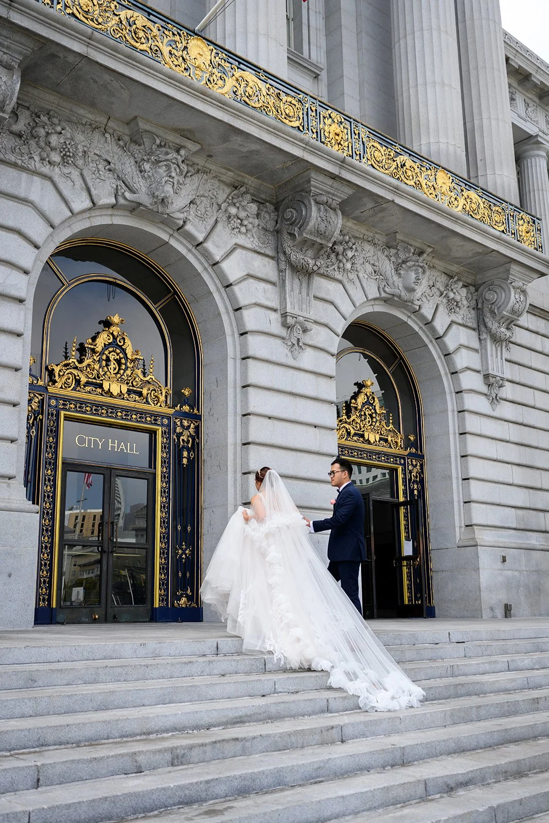 A bride and groom walking up the stairs to san francisco city hall on their weddings day