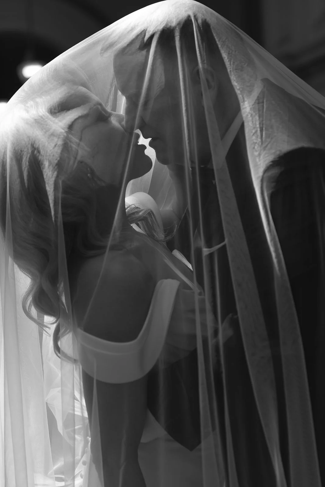 Black and white photo of a woman and a man kissing, partially obscured by a sheer fabric curtain.