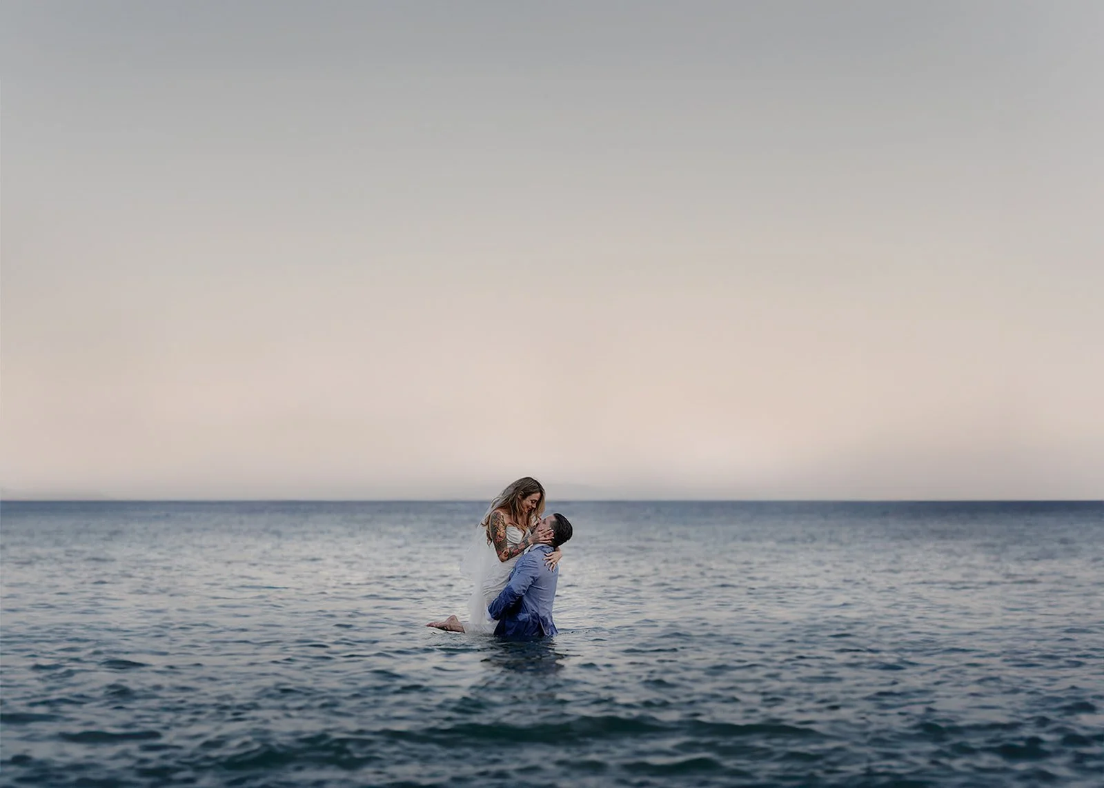 a bride in groom in their wedding outfits in the ocean in Greece at sunset