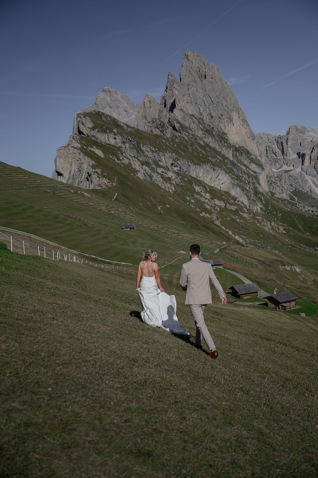 A wedding in the dolomites where the groom is chasing the bride through a field on a mountain in Italy