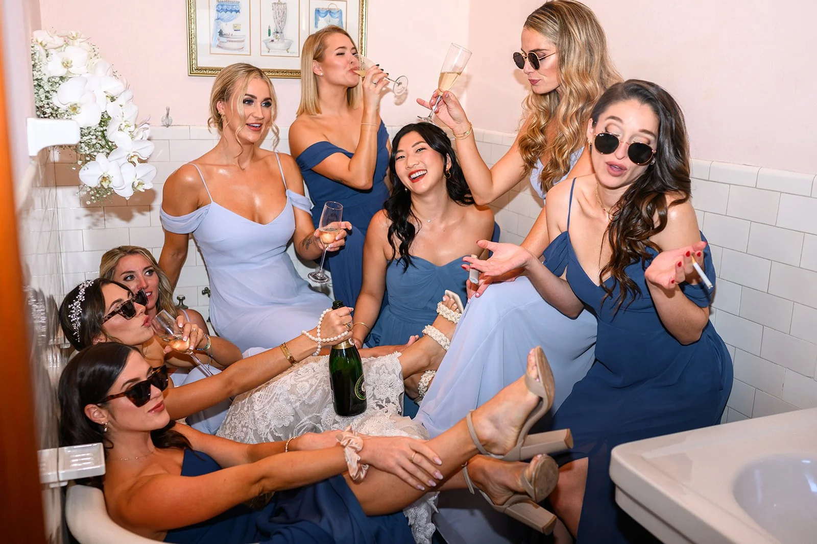 a photo of a bride and all her bridesmaids in a bathroom and in a tub drinking champagne and partying