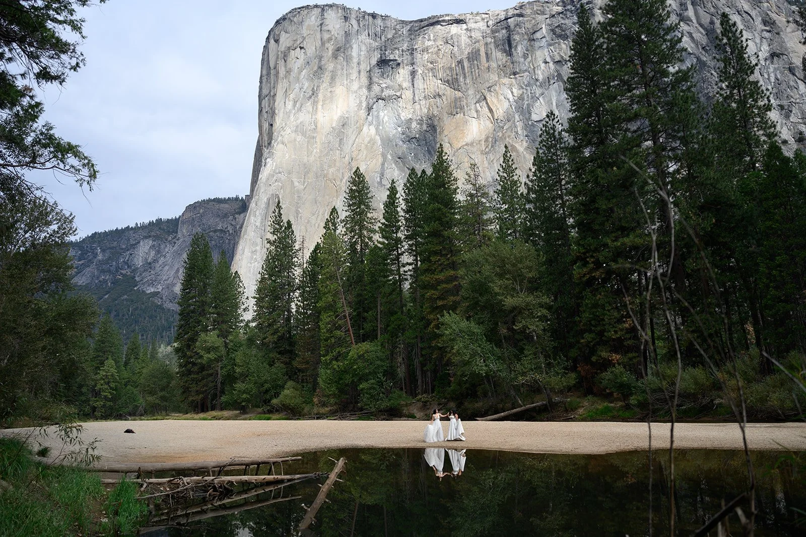 a photo of two brides in yosemite valley with el capitan behind them and their reflections in the water