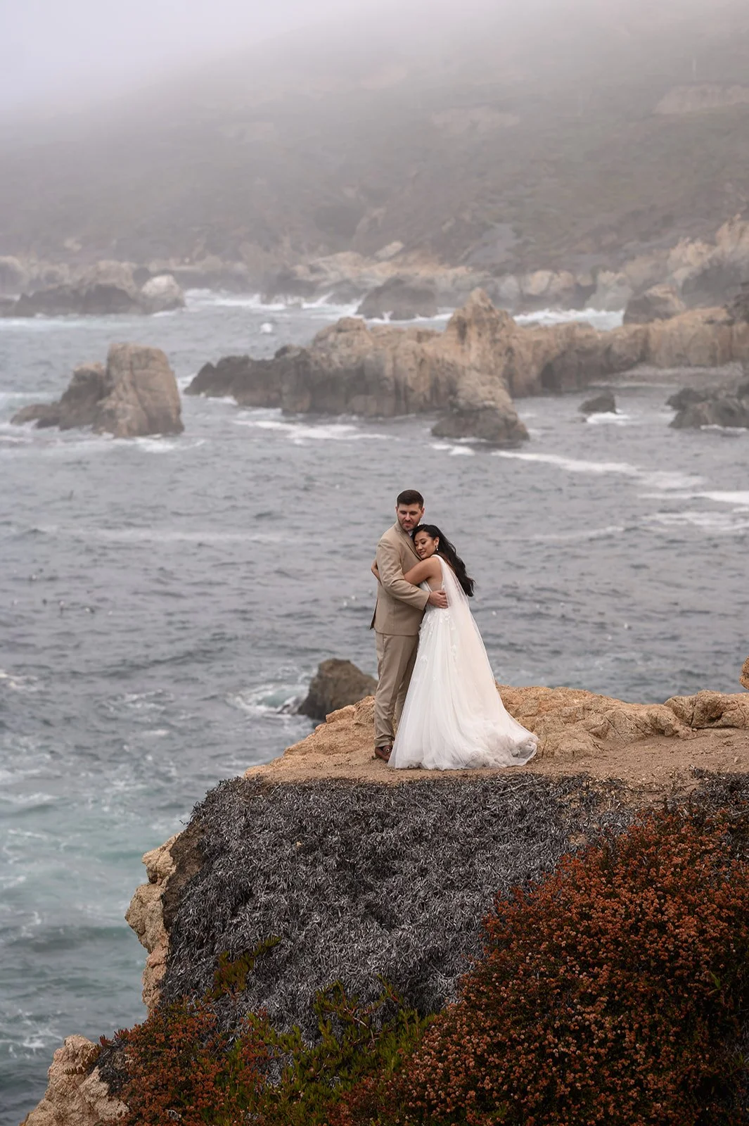 A bride and groom standing on a cliff at Big Sur on their wedding day