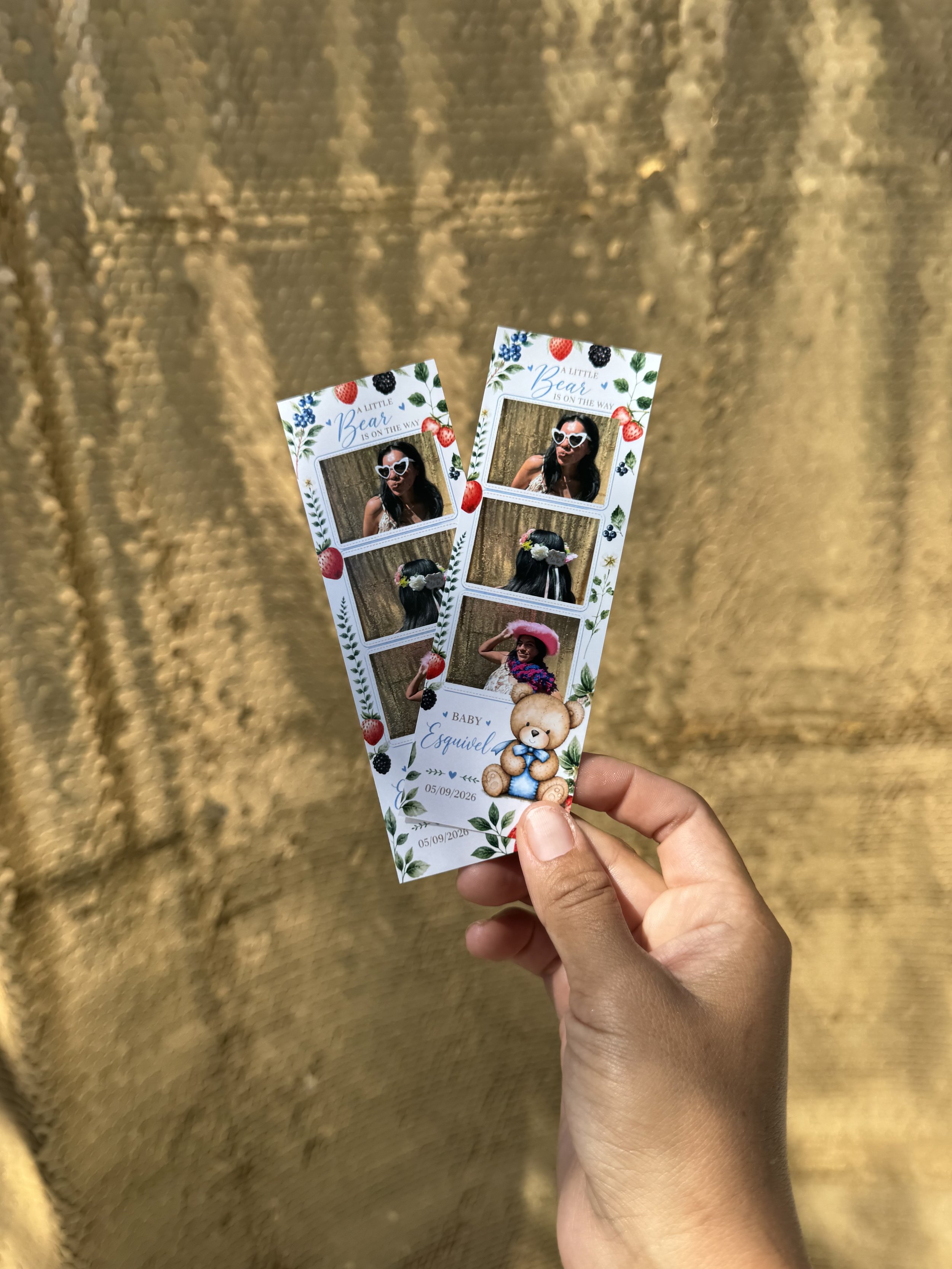 Two photo booth strips held in a person's hand, featuring images of a woman wearing sunglasses and various outfits, with a gold background.