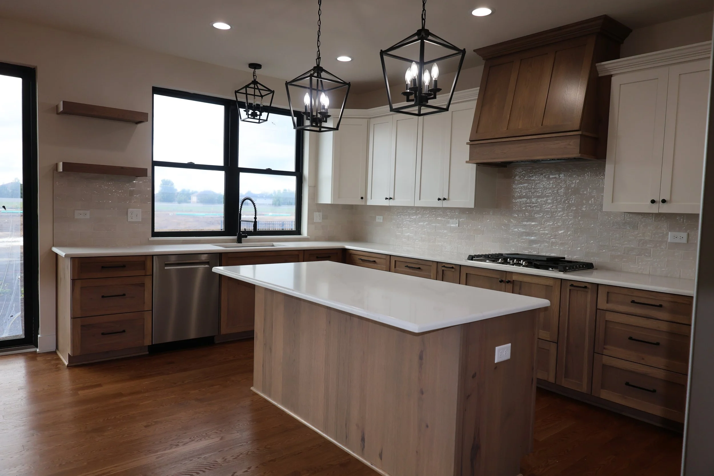 Modern kitchen with white cabinets, wood accents, an island with a white countertop, pendant lighting, and large windows.