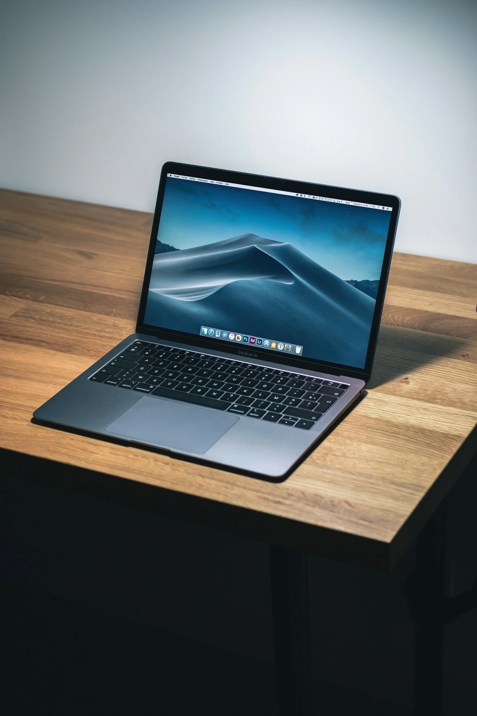 A silver MacBook Air laptop open on a wooden desk, displaying a desert scene on the screen.