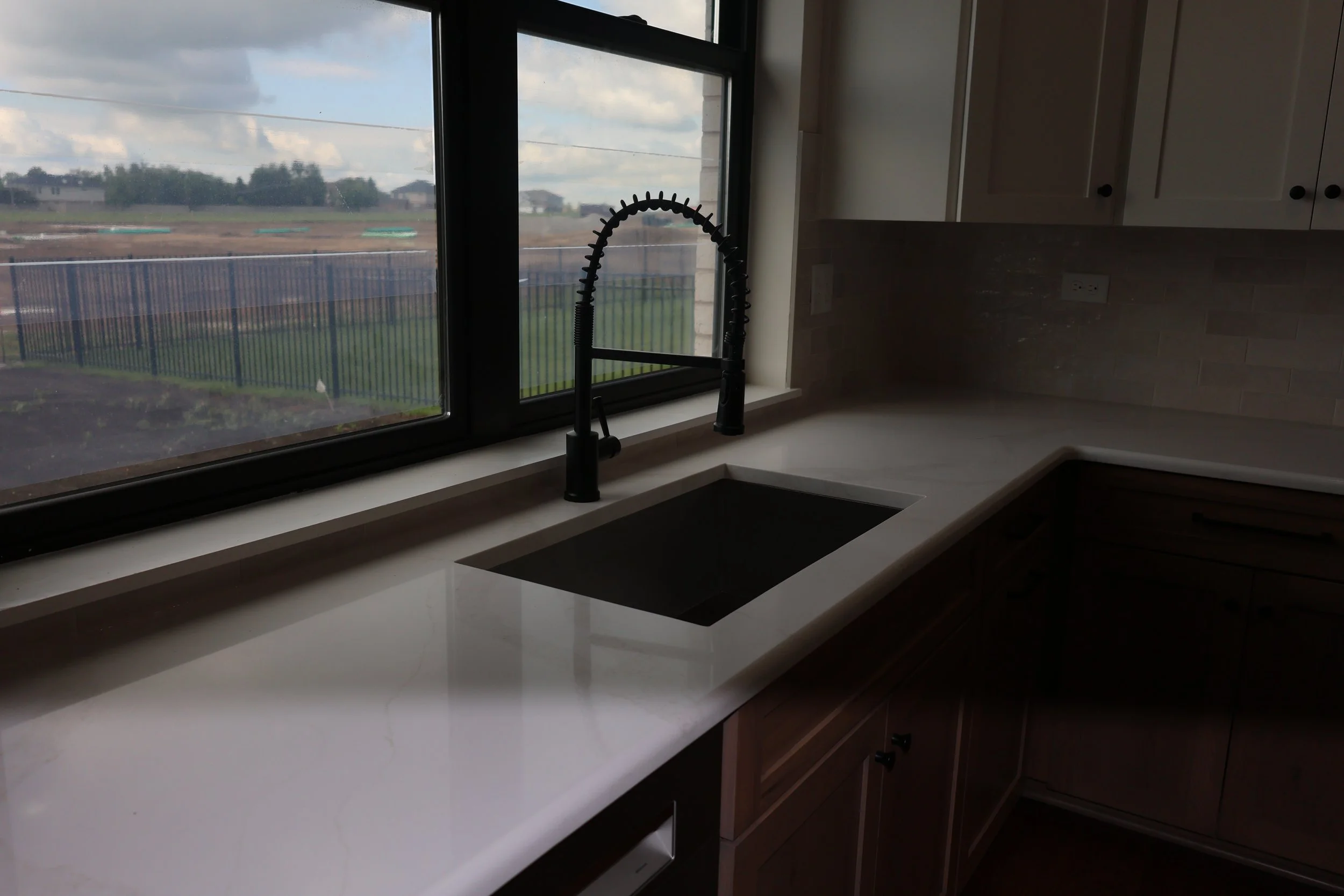 Kitchen with a white countertop, black sink, and black spring kitchen faucet, overlooking an outdoor view through a large window.