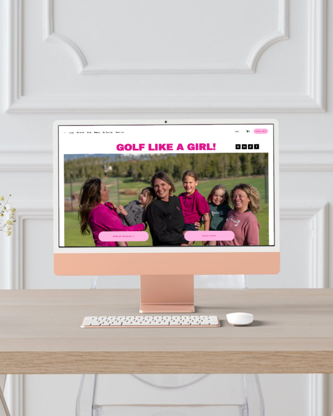 A computer monitor on a desk displaying a website titled 'GOLF LIKE A GIRL!' with a group of women and girls smiling outdoors on a golf course.