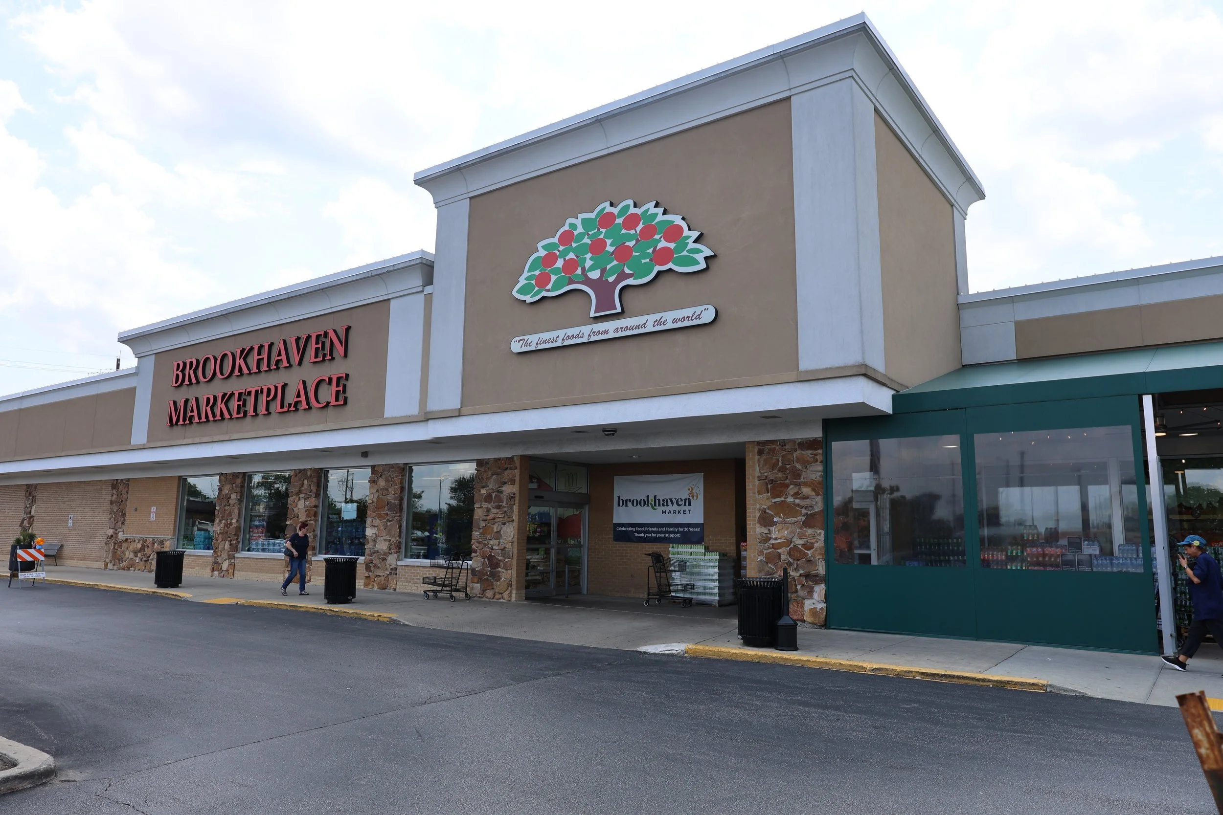 Exterior of Brookhaven Marketplace with signage, stone accents, and a woman walking outside.