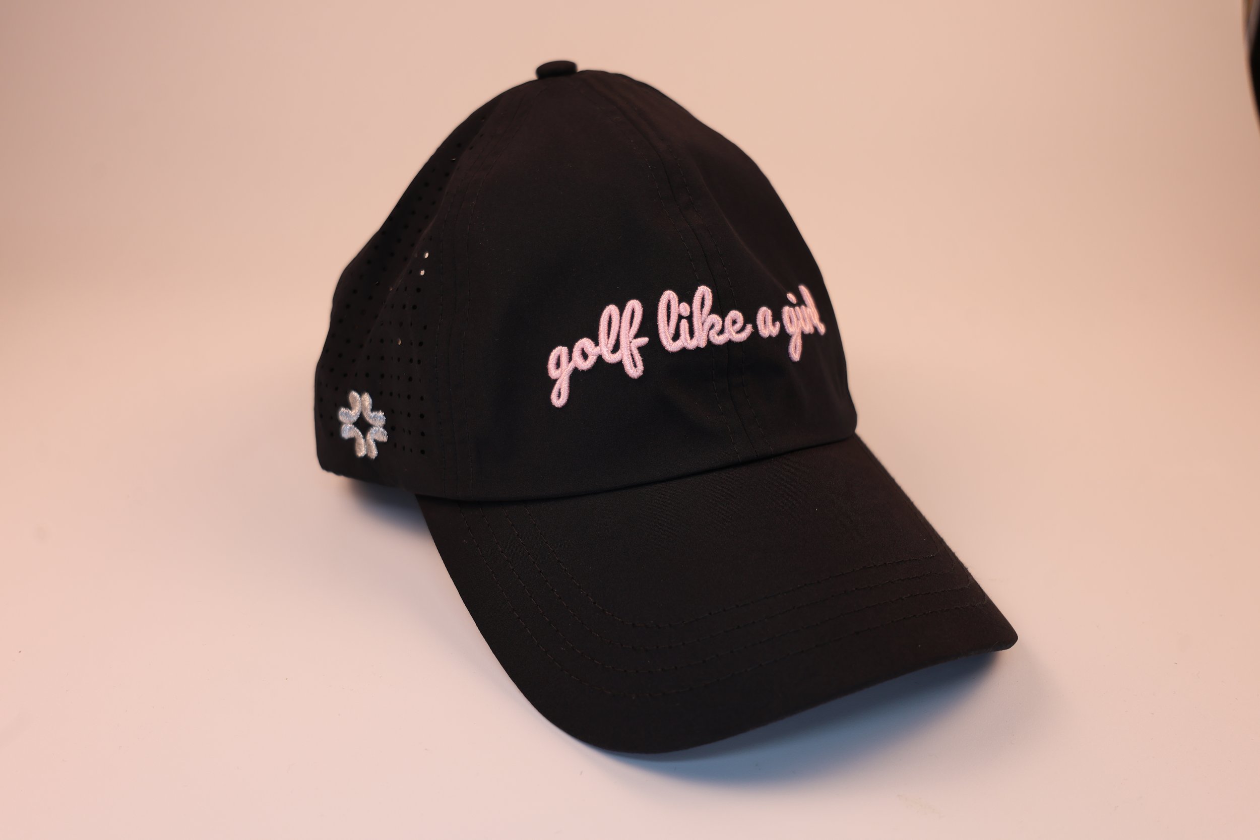 Black baseball cap with pink embroidered text 'golf like a girl' and a small white logo on the side.