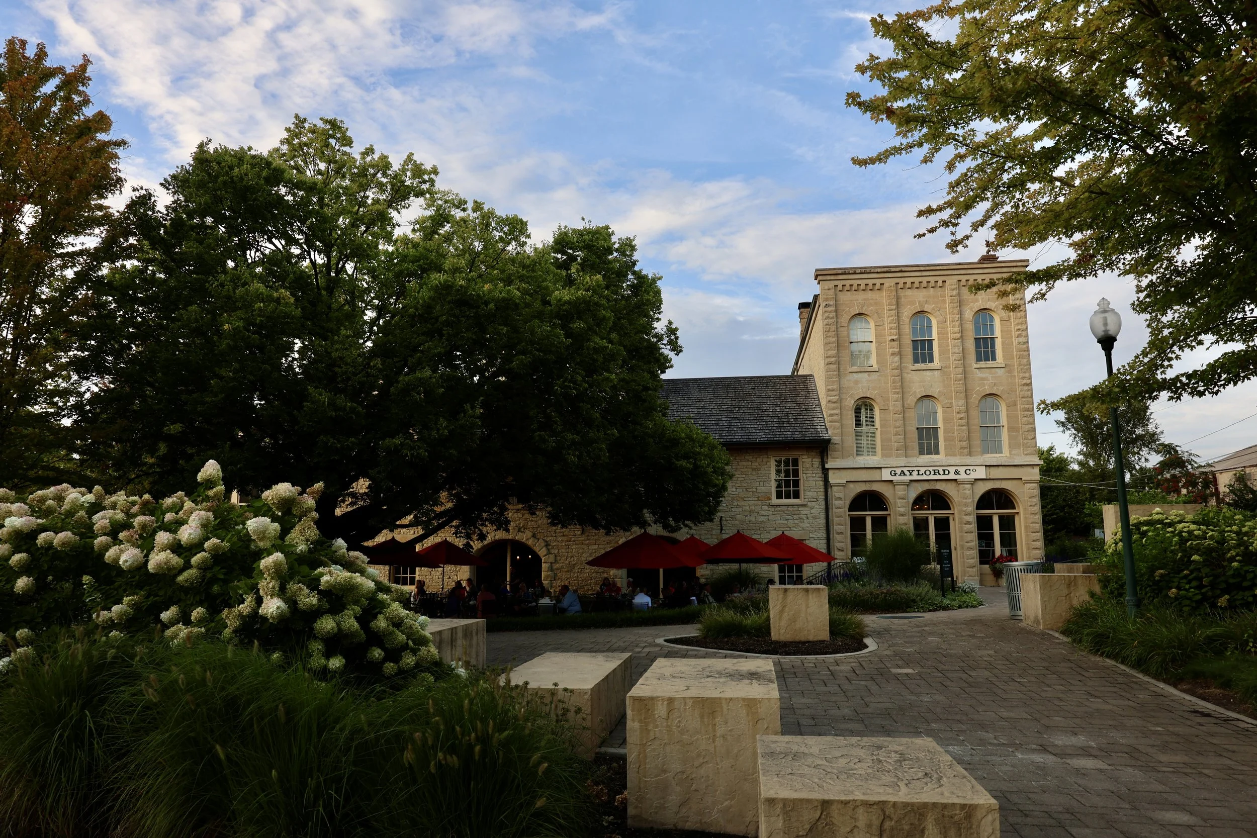 A historic building labeled GAYLORD & CO with outdoor seating, green trees, and a cloudy sky.