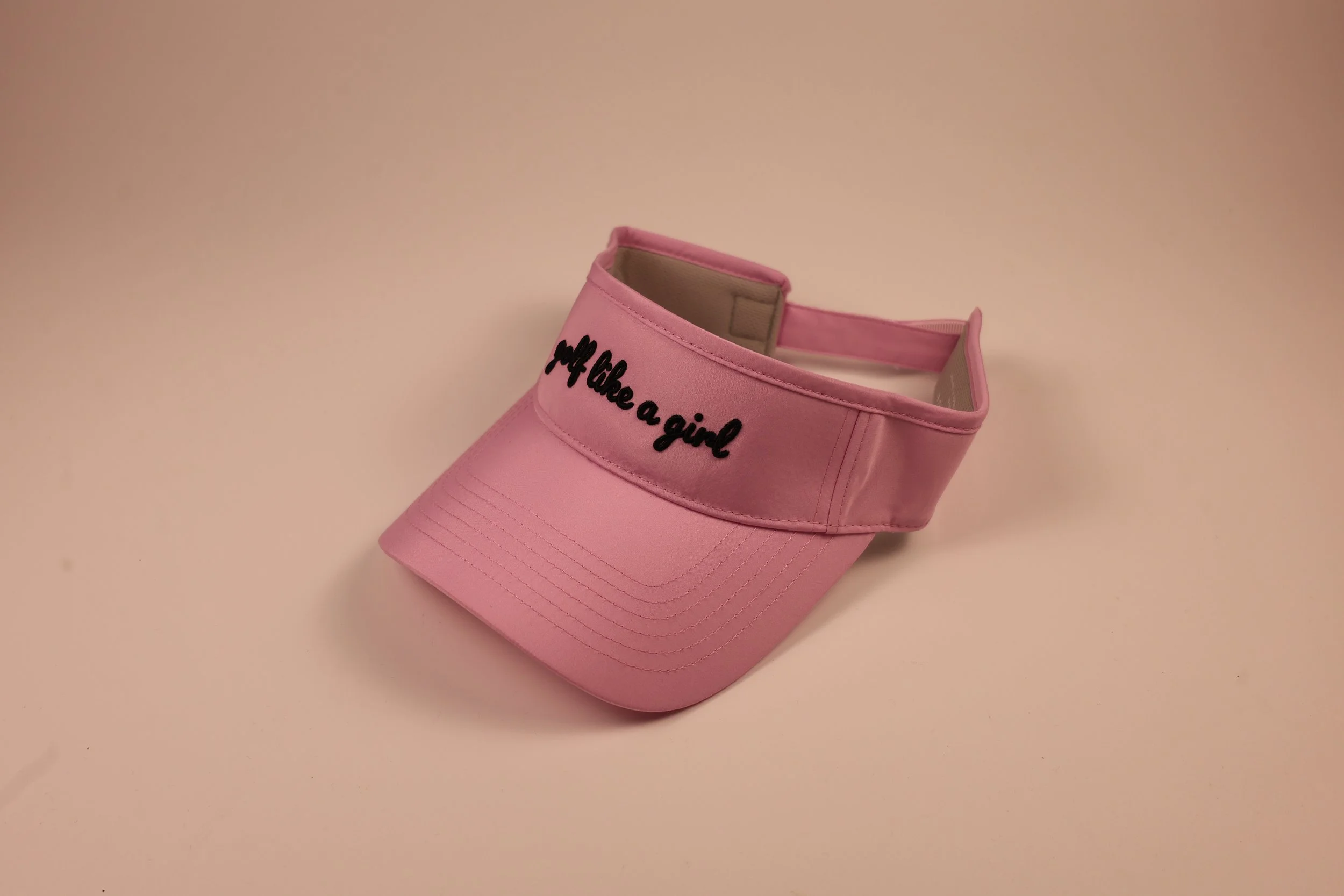 Pink visor cap with the words "Wall like a girl" embroidered in black on the front.