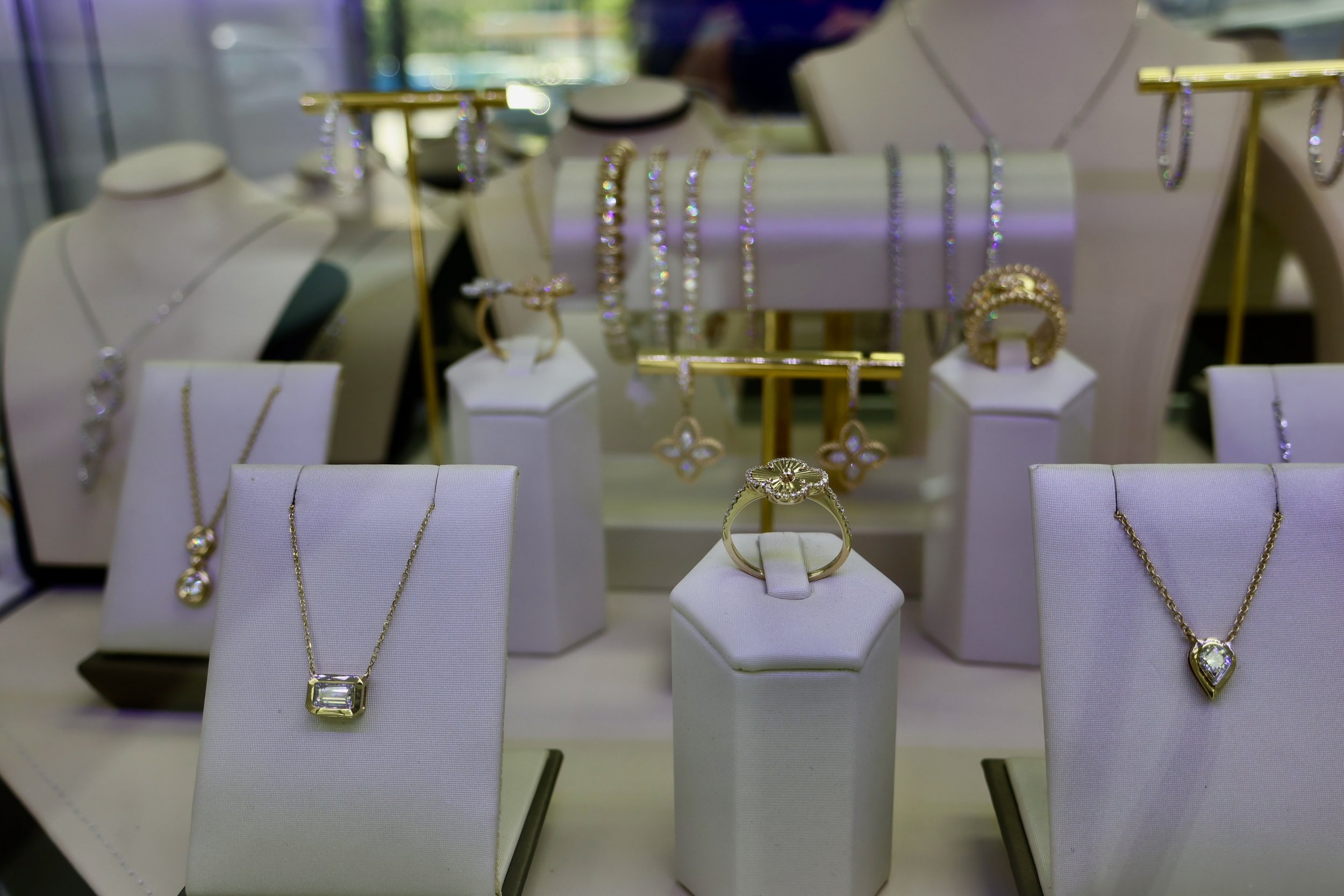 Display of gold jewelry including necklaces, rings, and earrings, showcased on white stands and platforms at a jewelry store.
