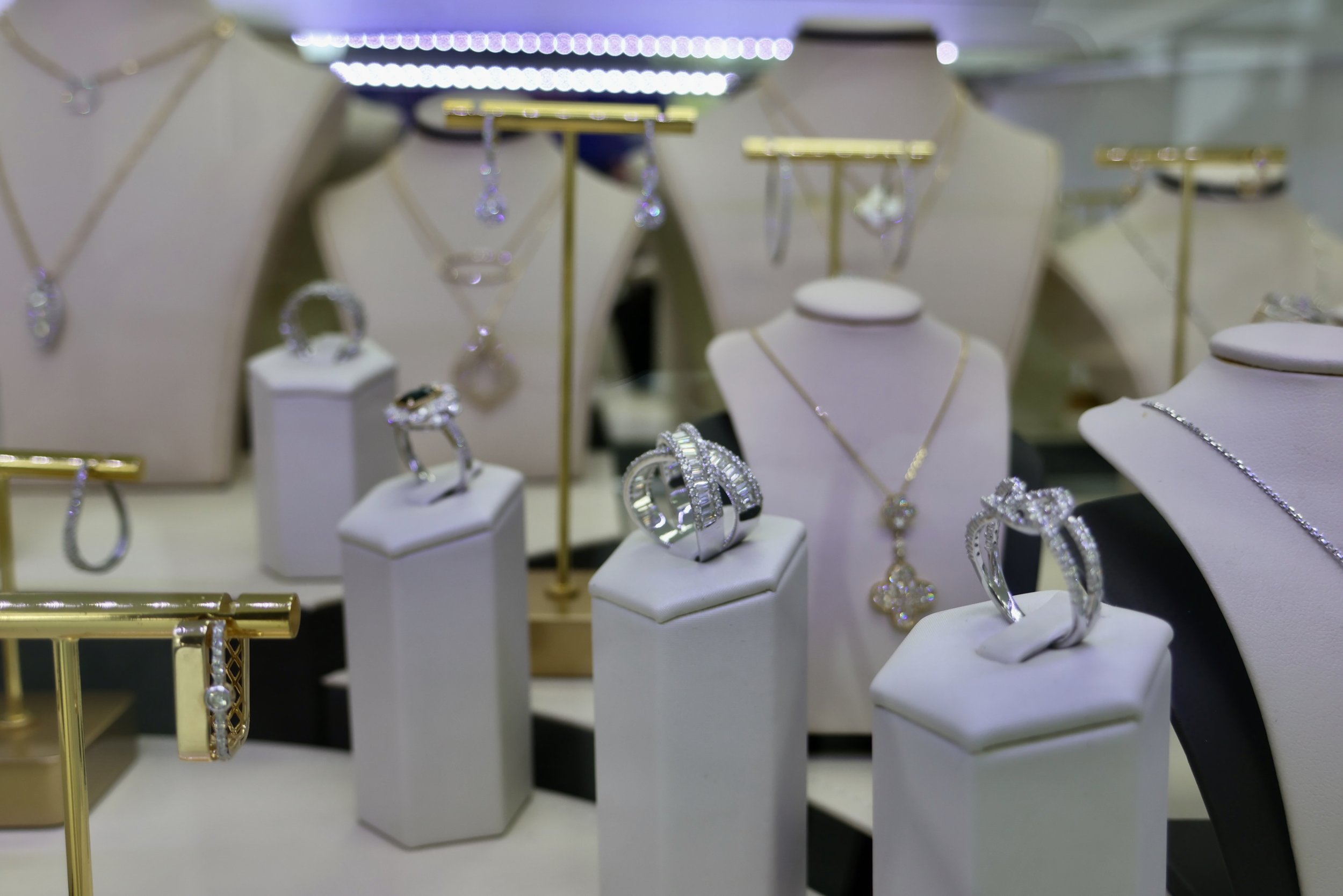 Jewelry display with rings, necklaces, and earrings in a jewelry store showcase, with white and black busts and stands, and gold accents.
