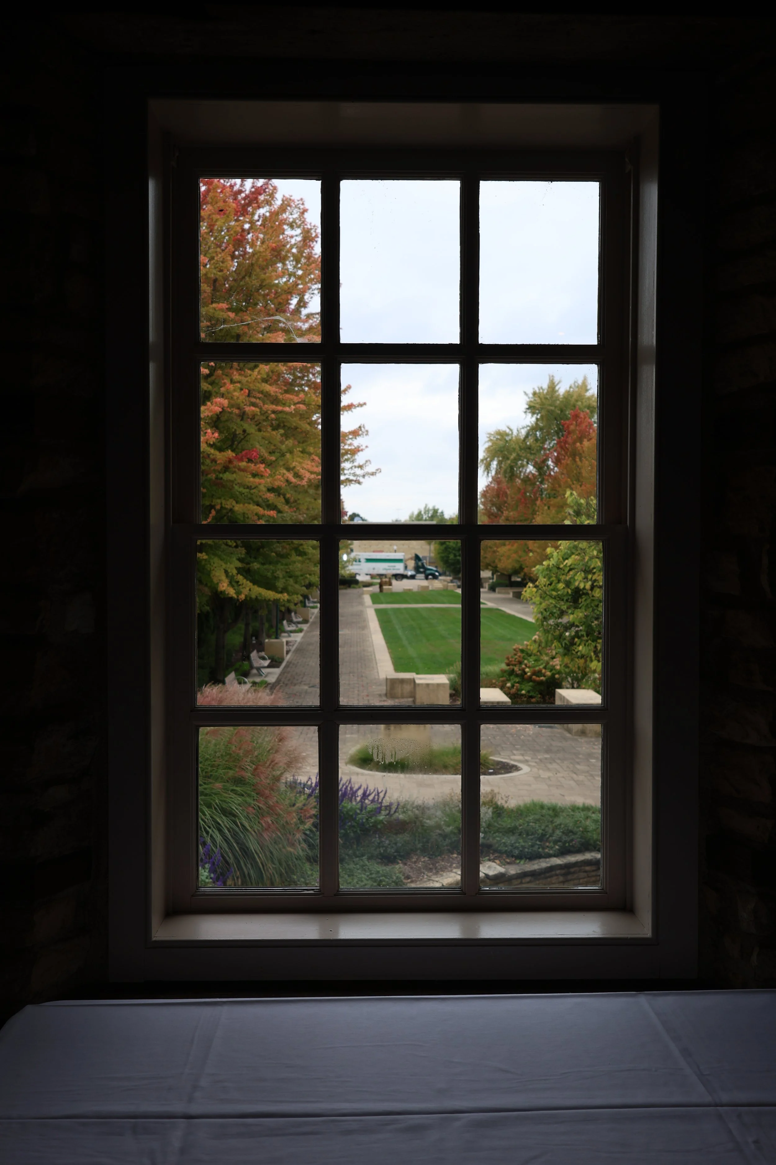 View of a landscaped park with trees in autumn colors through a window with divided panes.