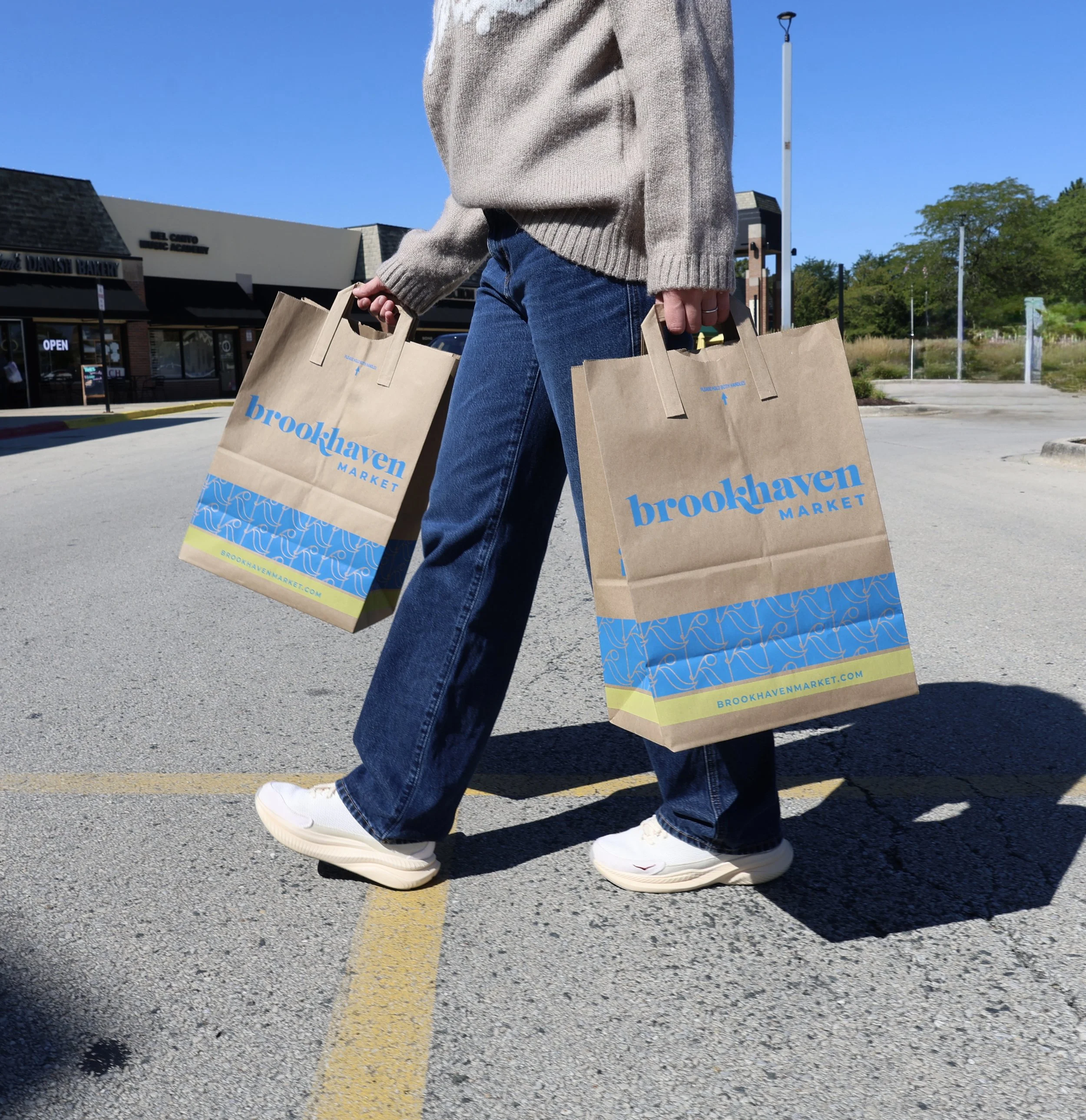 Person walking in parking lot carrying two paper shopping bags from Brookhaven Market.