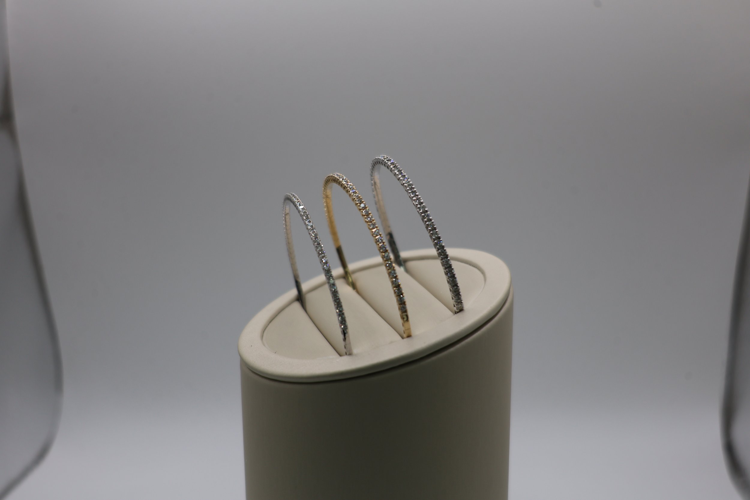 Three diamond-studded rings, one silver, one gold, and one platinum, displayed on a white ring holder.