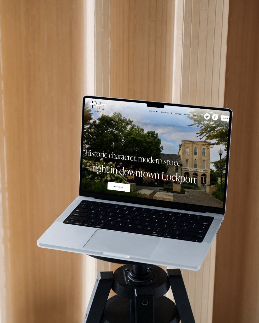 A laptop on a tripod stand displaying a website about Lockport with a historic building in the background.