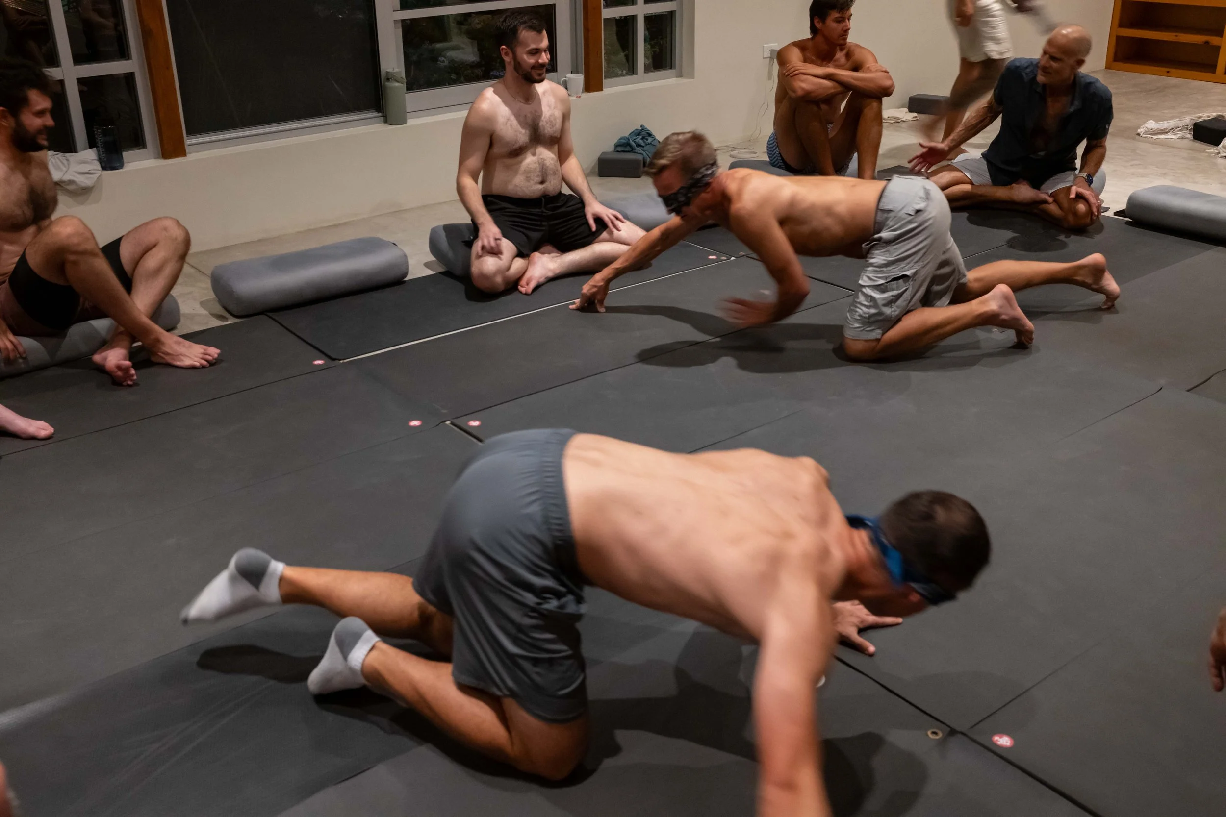 Men exploring a playful embodiment exercise on mats indoors at SHIFT Men’s Retreat, a somatic retreat for men that fosters trust, presence, and emotional growth.