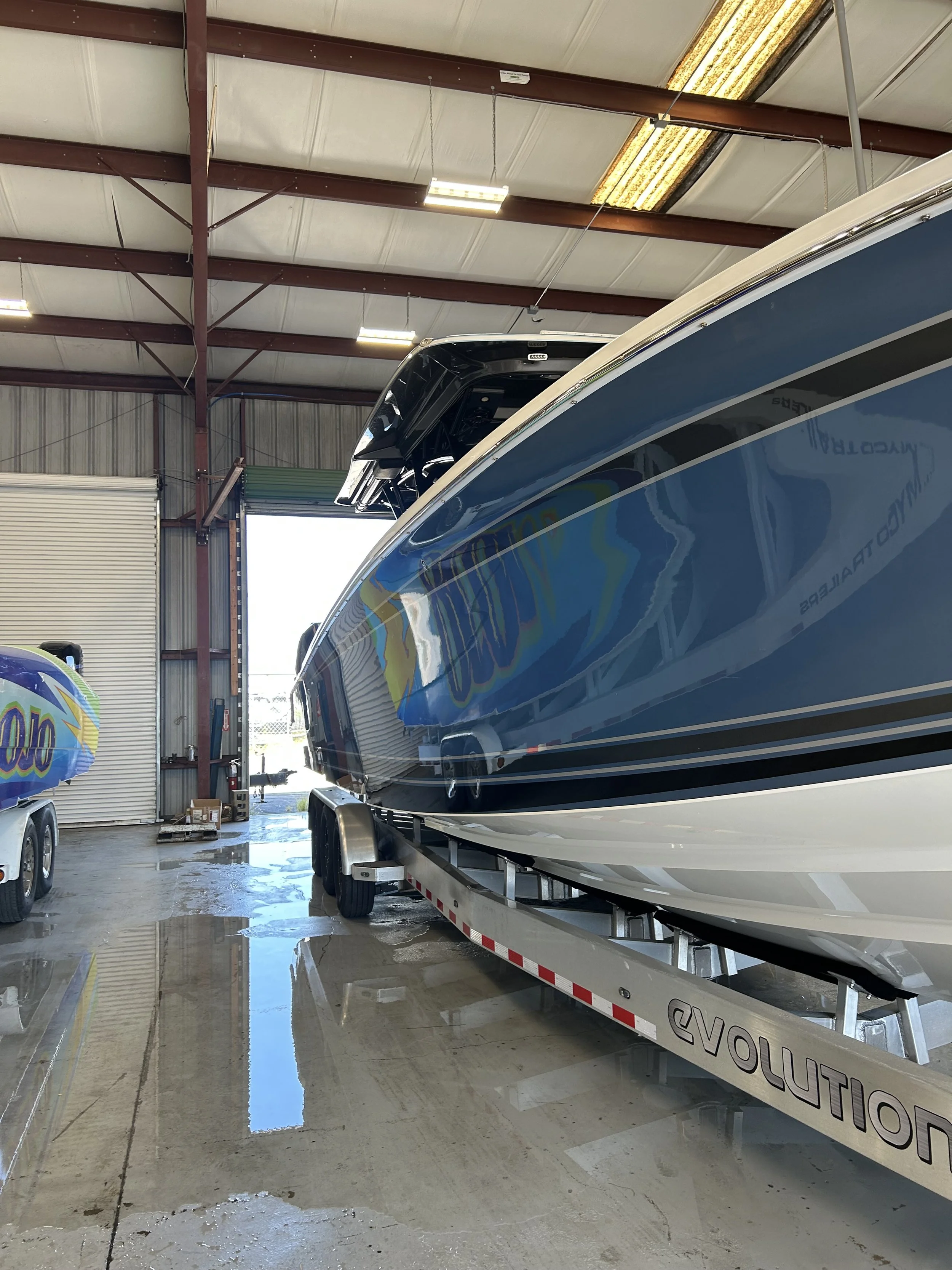 A blue and white speedboat on a trailer inside a warehouse. The boat is labeled 'Revolution' on the trailer.