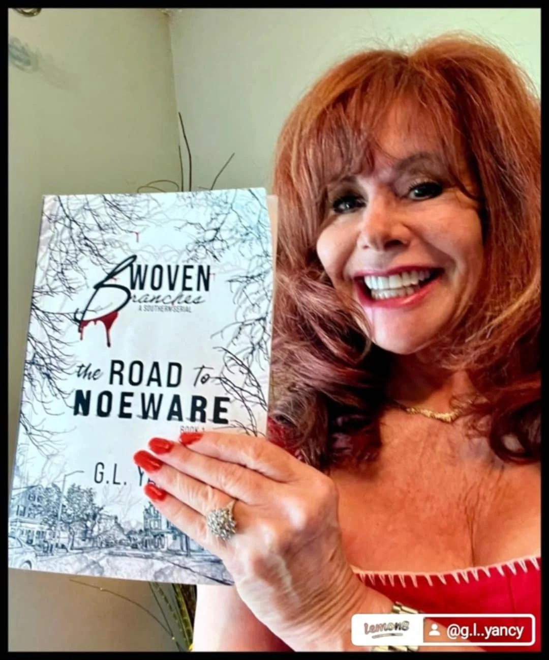 A woman with red hair holding a book titled 'The Road to Noeware' by G.L. Yancy, smiling at the camera.