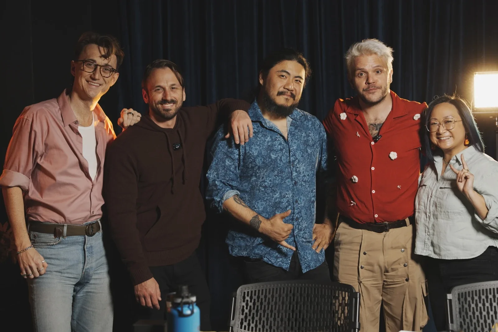 Group of five diverse individuals posing for photo on stage, with dark curtain background and bright stage light to the right. Production still from the Best Interview Ever Youtube show.