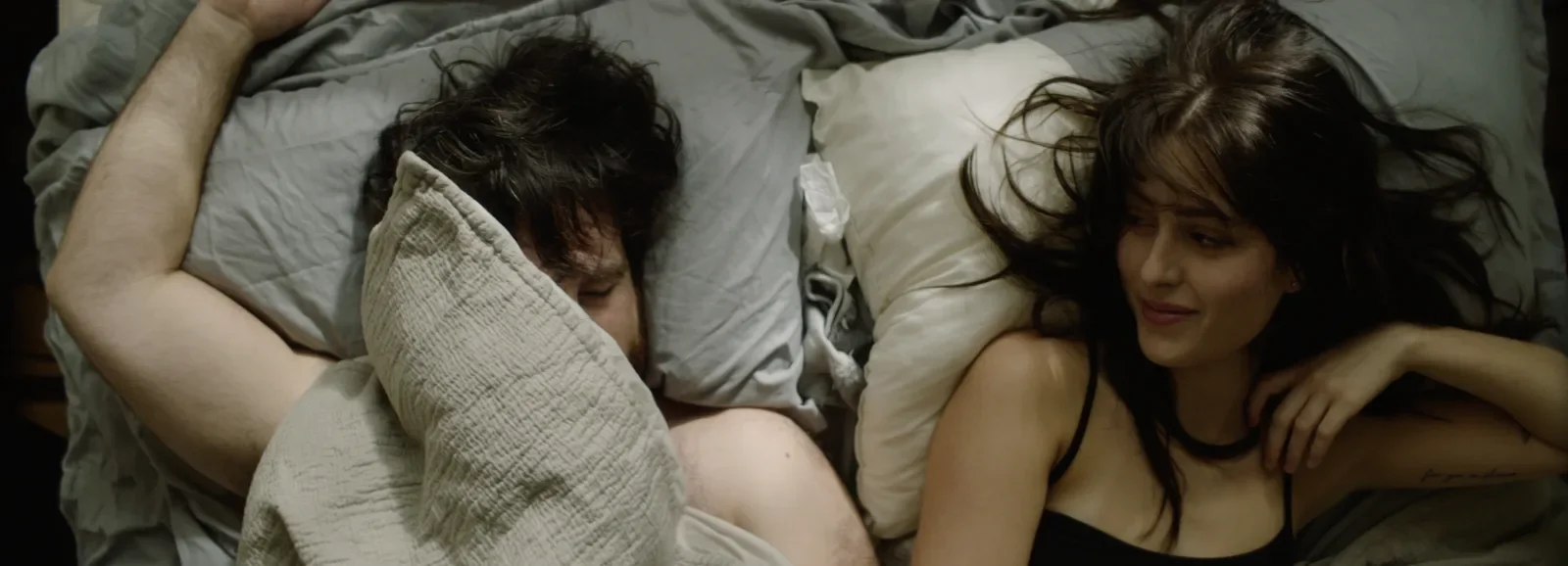 A young man and woman lying in bed, close to each other. Production still from Bad Seed.