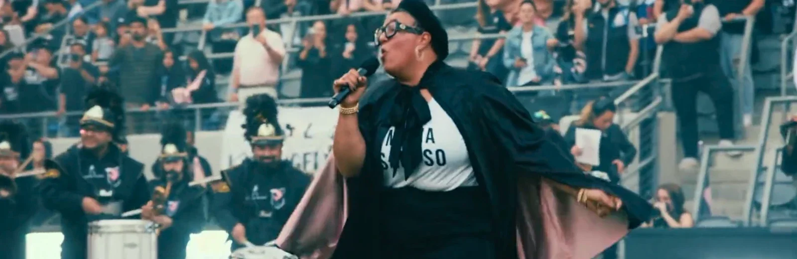 A woman speaking into a microphone at an indoor event with people seated in the background. Production still from Johnnie Walker commercial.