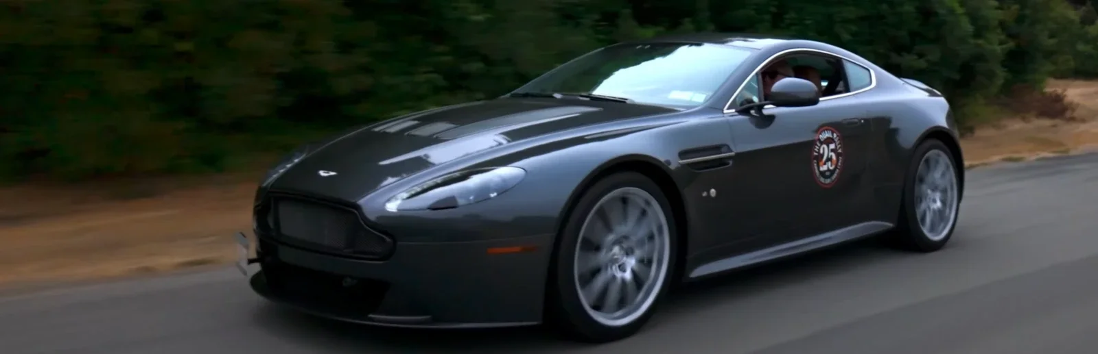A black sports car driving on a road with trees in the background. Production still from The Quail Rally commercial.