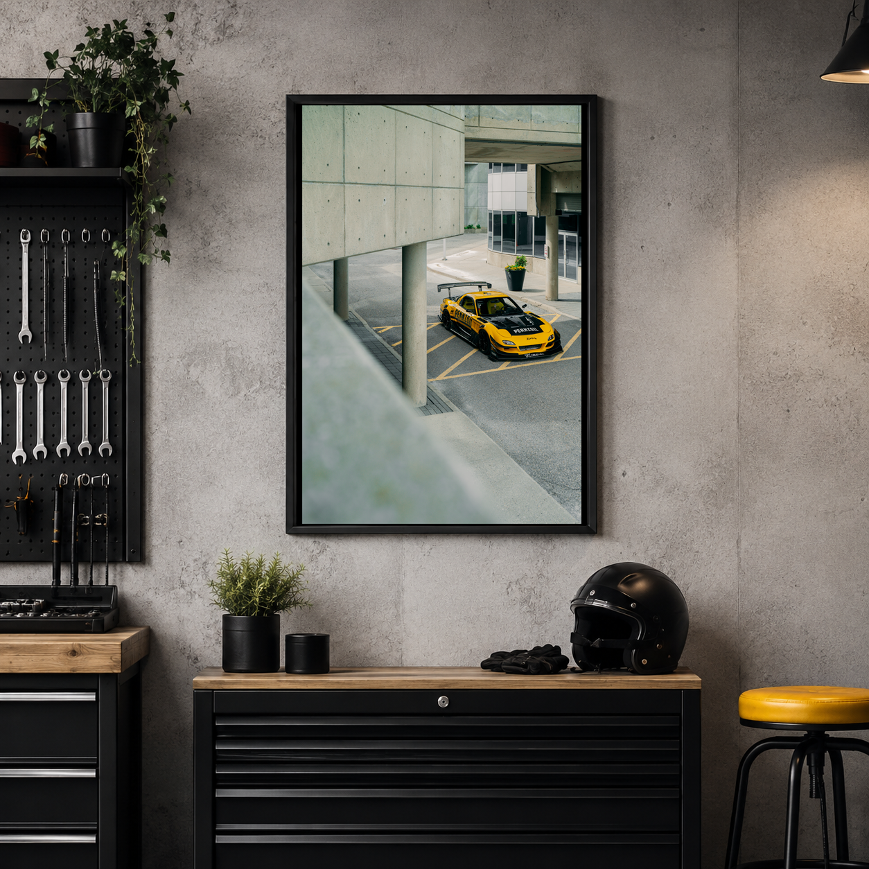Interior of a garage with a photo showing a yellow Mazda FD RX7 parked outside, tools on a black pegboard, potted plant, helmet, and black stool.