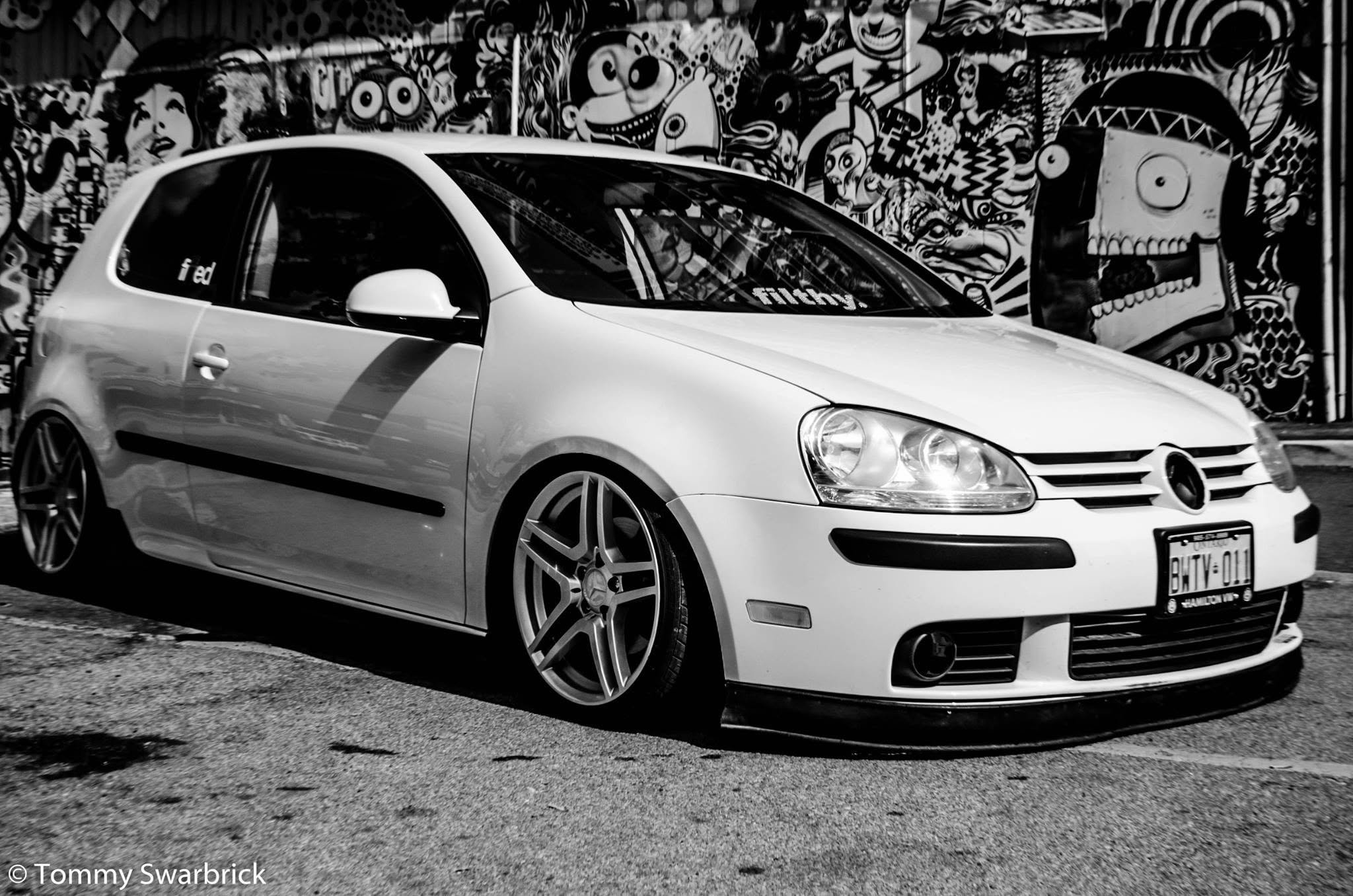 A white sports car parked in front of a colorful, graffiti-covered wall.