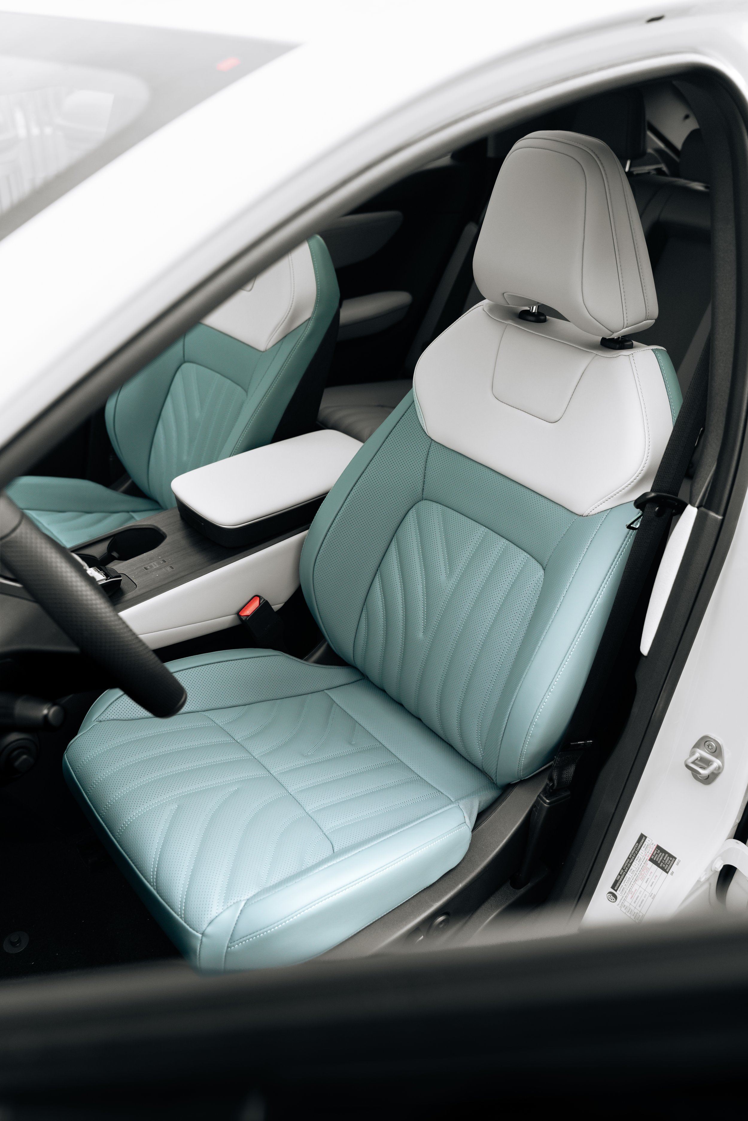 Front passenger seat inside a modern white car with teal and white leather upholstery, visible headrest, and part of the center console.