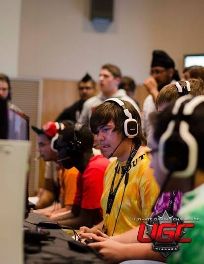 Group of gamers, mostly young men, wearing headphones, focused on computer screens in an indoor gaming tournament with the LGC logo in the bottom right corner.