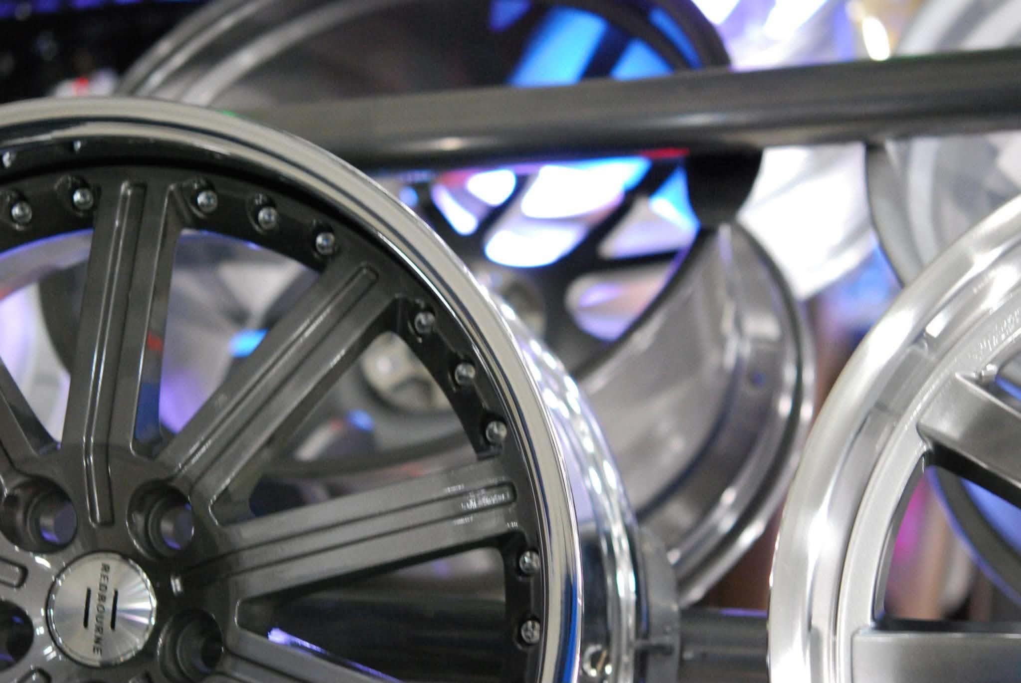 Close-up of multiple stacked black and silver wristwatches with metallic bands and round watch faces, illuminated by blue and purple lighting.