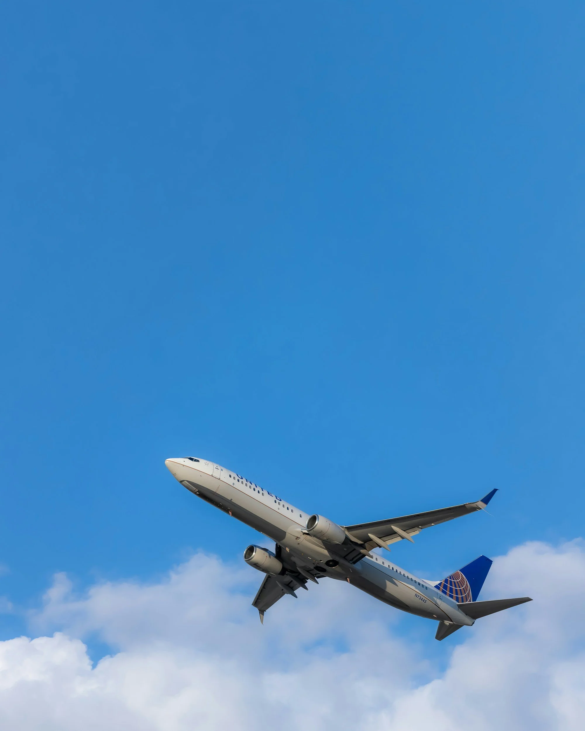 United Airlines commercial airplane flying through a partly cloudy blue sky.