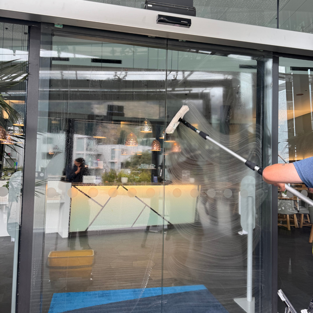 Commercial interior window cleaning with a squeegee removing fingerprints and marks from glass doors.