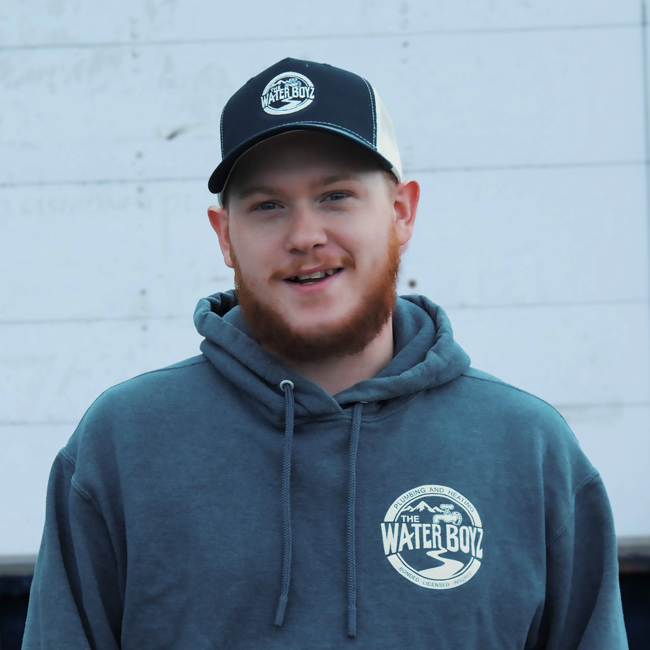 Close-up of a young man wearing a blue hoodie and a black and white baseball cap with a logo that says "The Water Boyz" on the front.