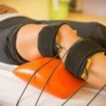 Person undergoing electrical muscle stimulation therapy with electrodes attached to their thigh.