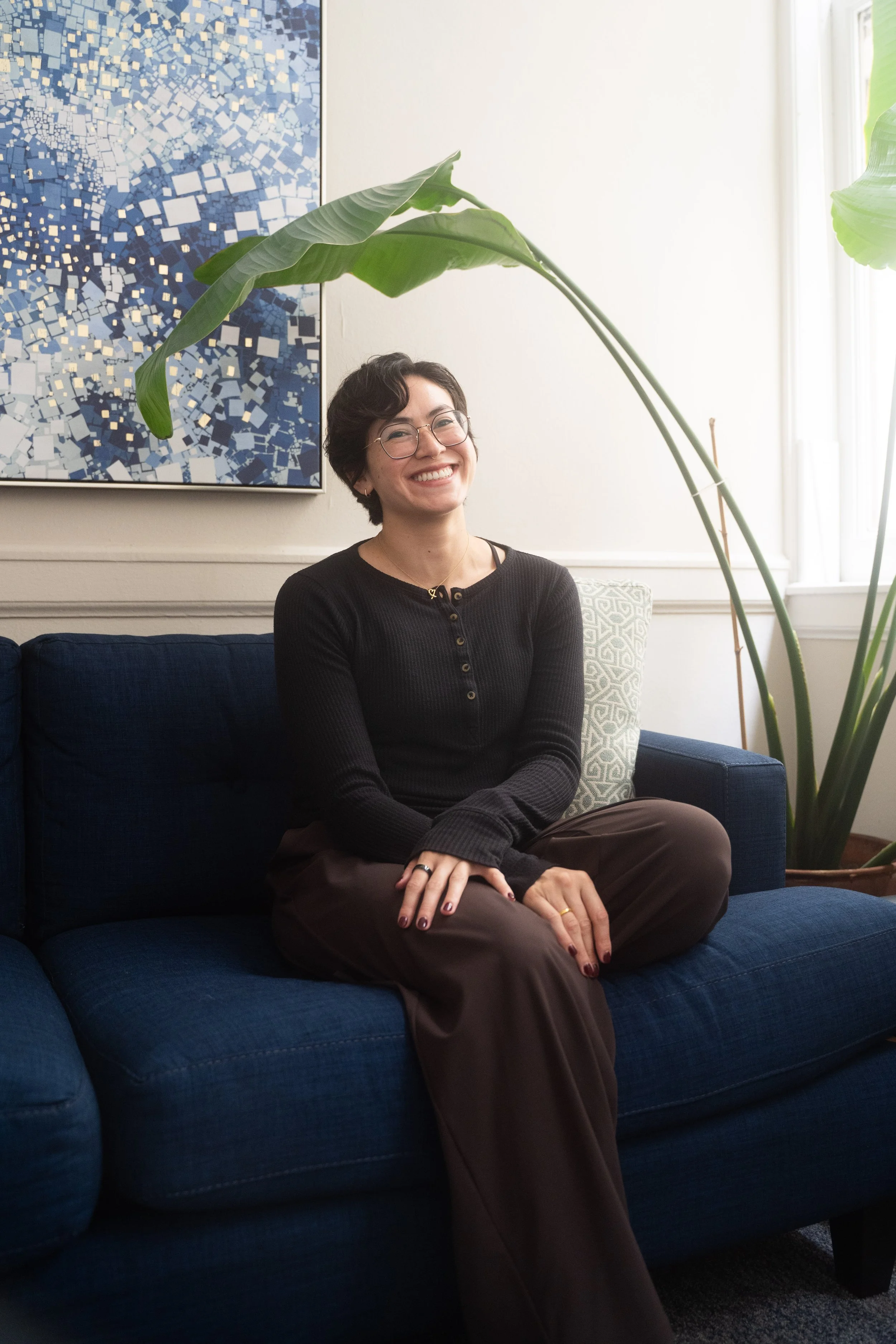 A photo of me sitting on a blue couch, with a plant nearby.
