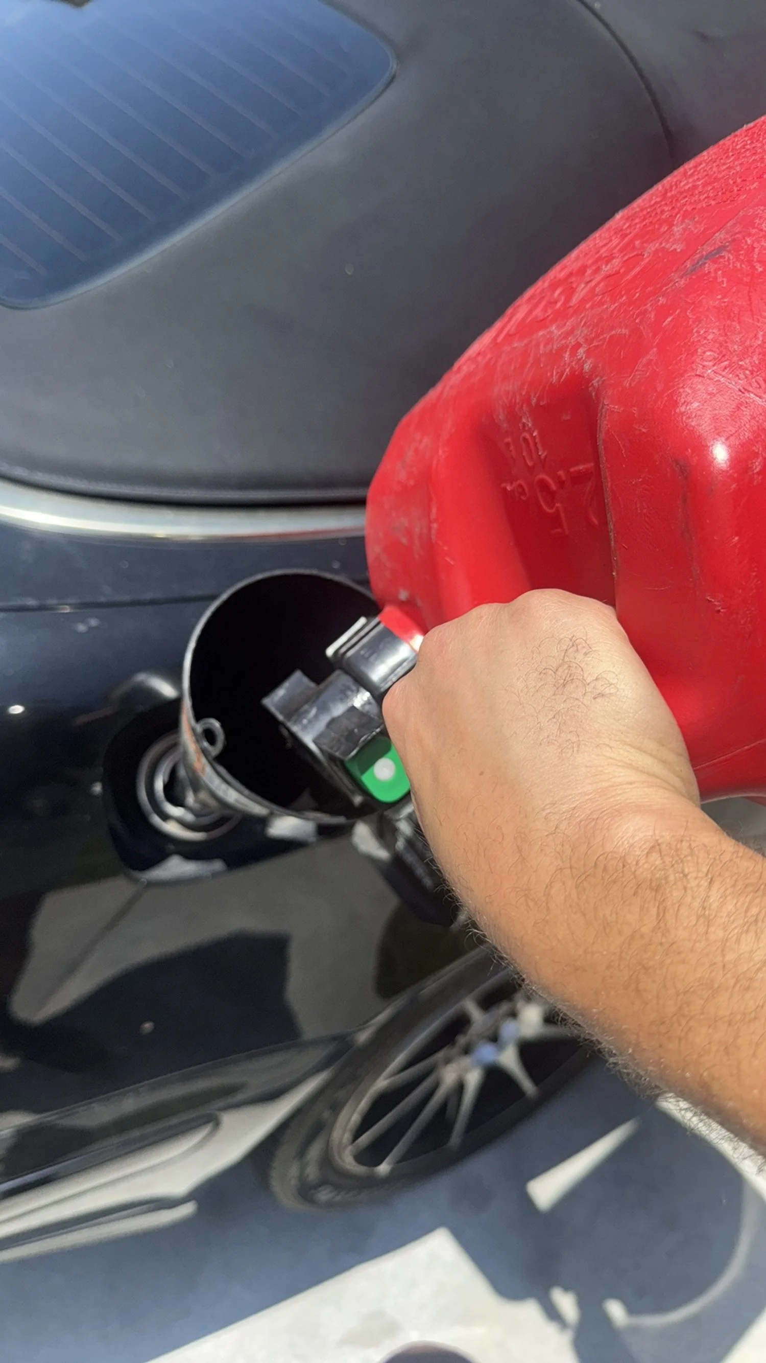 A person holding a red gasoline can pouring fuel into a scooter's fuel tank.