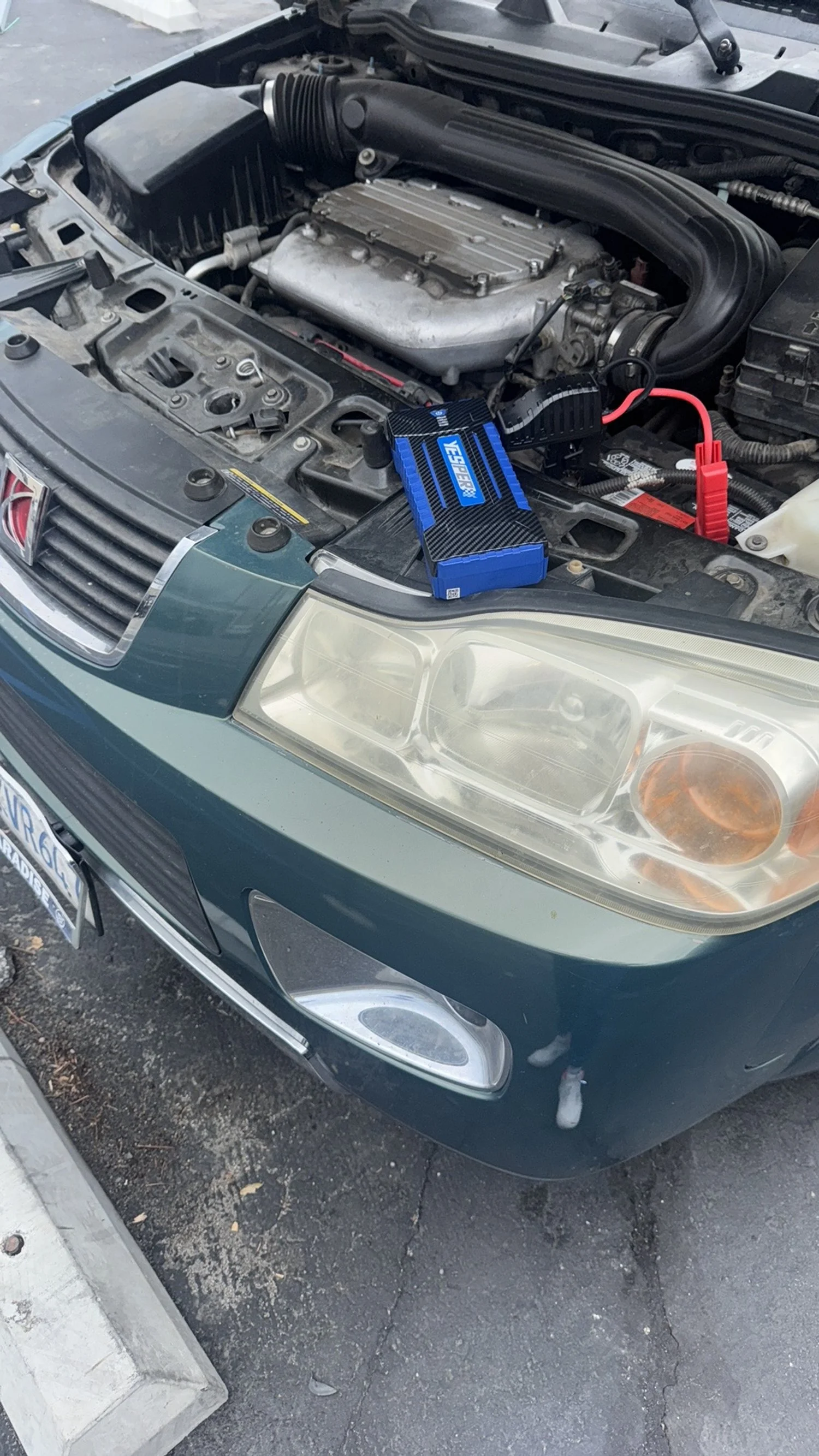 Car with open hood, showing engine and an electric jump starter on the front edge of the engine bay.