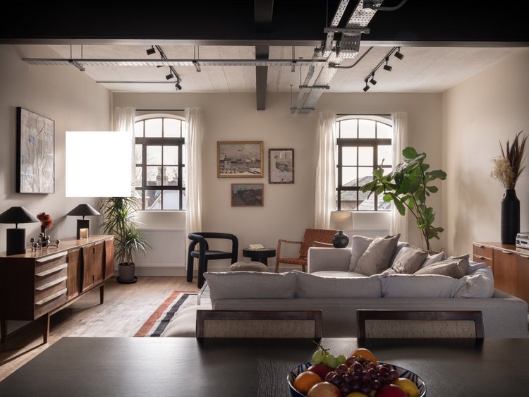 Bright living room with large windows, white walls, wooden furniture, a cozy sofa, and decorative plants.