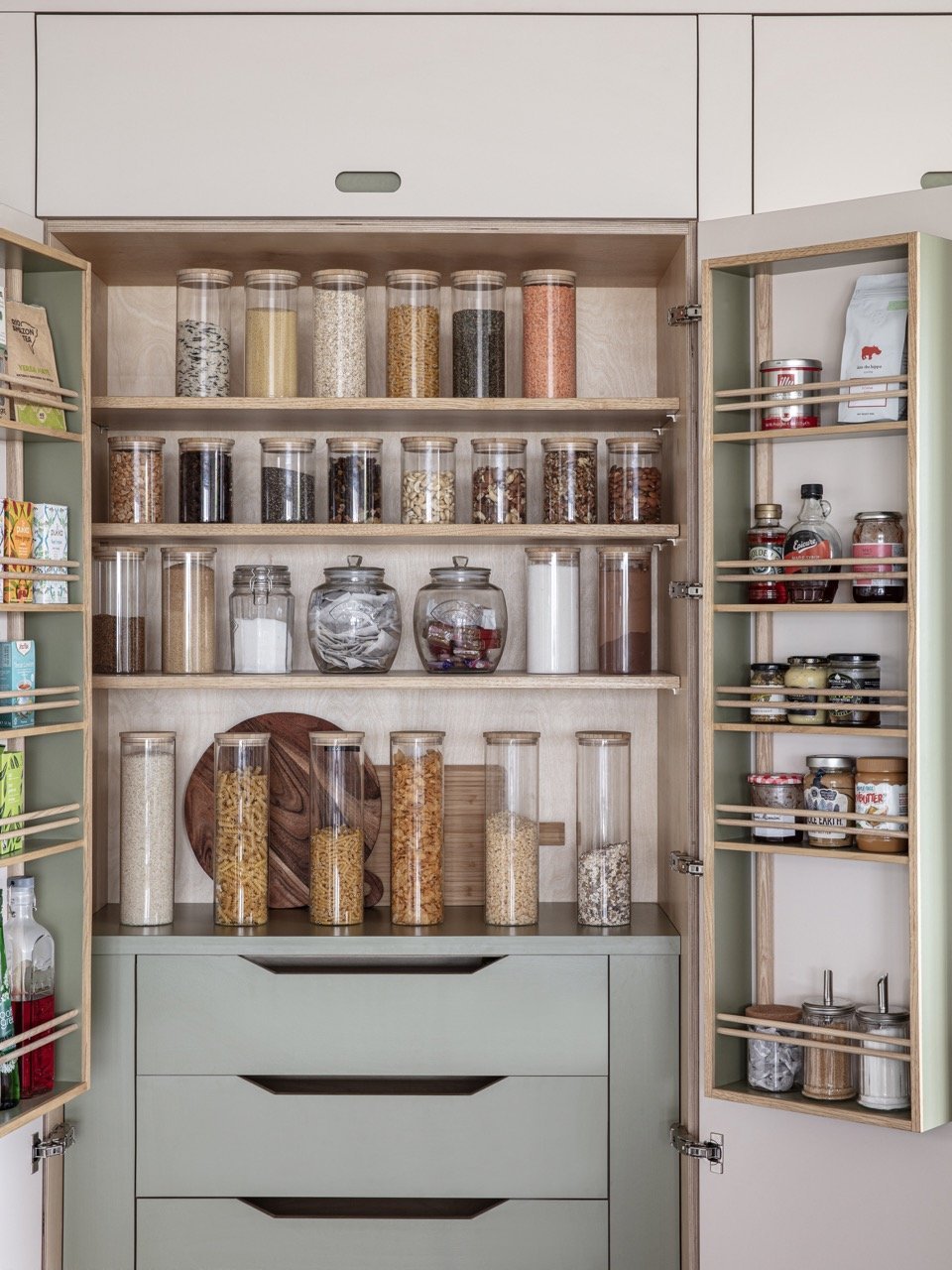 Open kitchen cabinet with glass jars filled with grains, pasta, and dried beans, and shelves with spices and condiments.