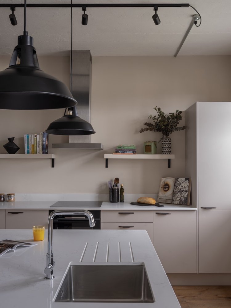 Modern kitchen with white cabinets, a white countertop island with a sink, black pendant lights, a glass of orange juice, and open books.