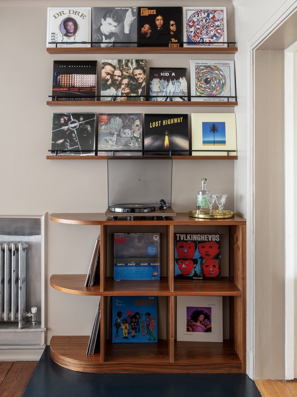 Shelf with vinyl records and a record player on a wooden storage unit, with wall-mounted shelves holding more records above.